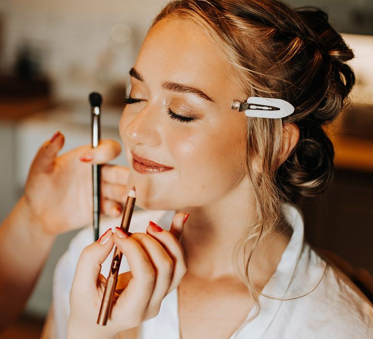 The bride sits getting her wedding makeup done for the barn wedding at Duddon Mill Farm 