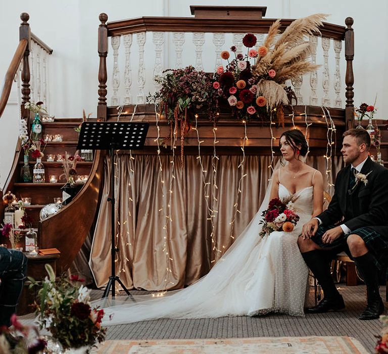 Bride in a Stephanie Allin bridal gown and groom in a kilt at their boho wedding ceremony decorated with fairy lights, wool rugs, wildflowers and pampas grass