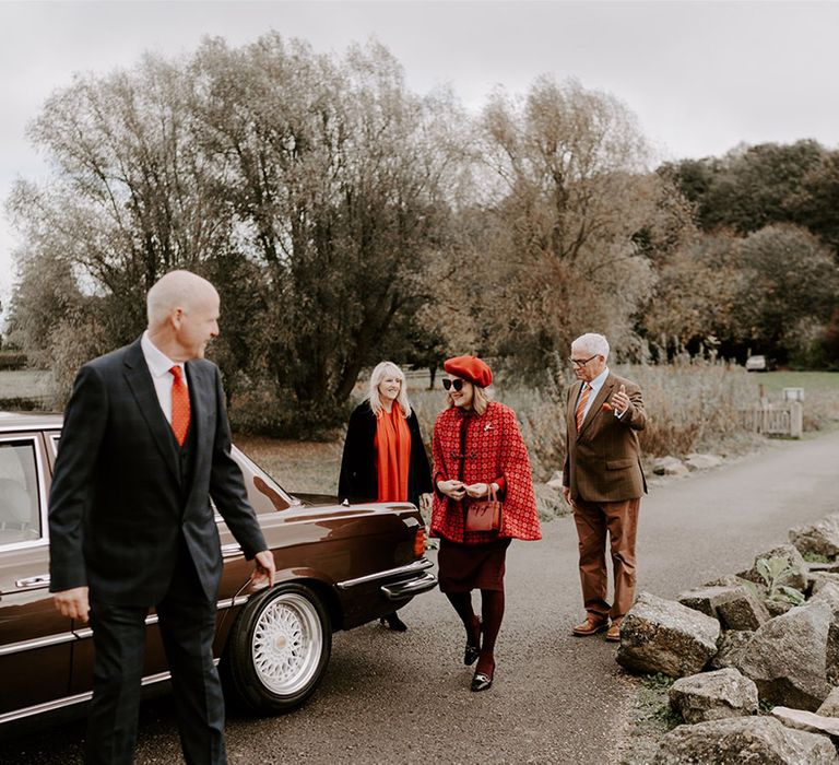 The wedding guests in red, brown, and orange autumnal theme wedding outfits arrive at the church for the wedding 