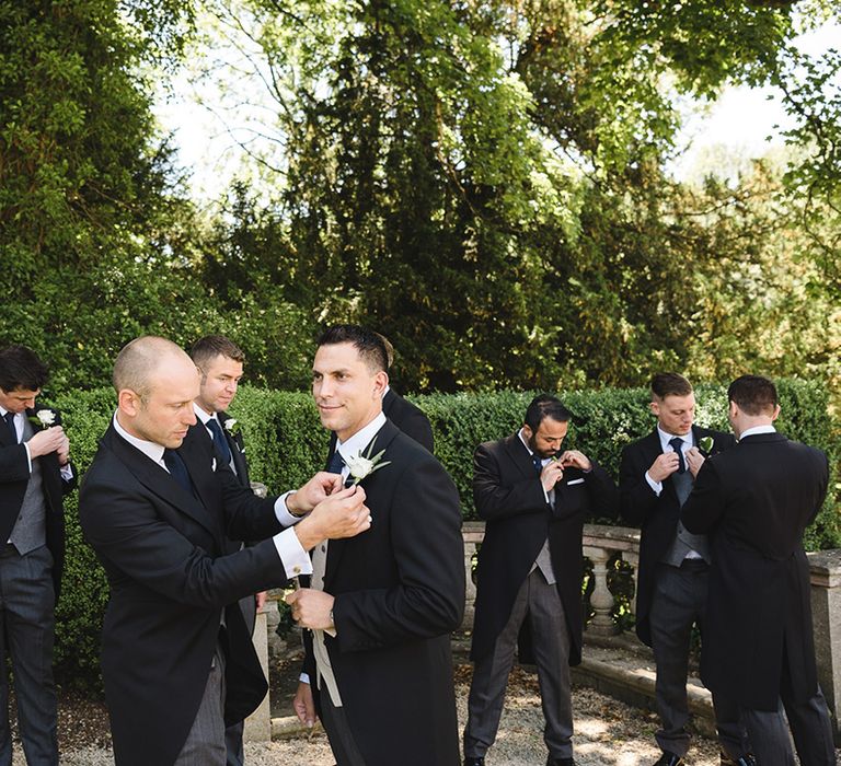 The groom and groomsmen all put on their white rose buttonholes for the classic country house wedding 