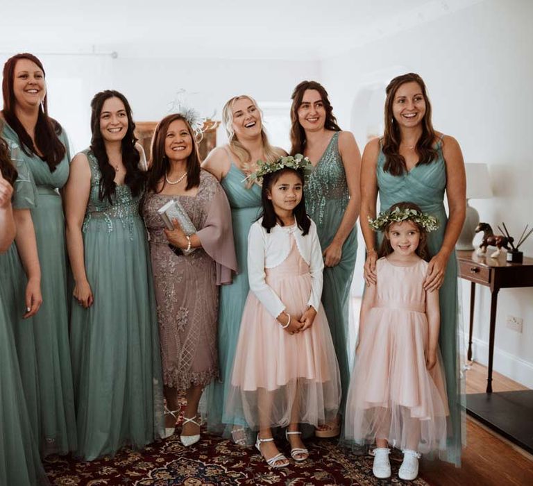 Bridesmaids in mismatched embellished teal bridesmaid dresses, mother of the bride in lilac embellished dress, lilac coverup and white fascinator and flower girl in baby pink dress with white cardigan and flower crown 