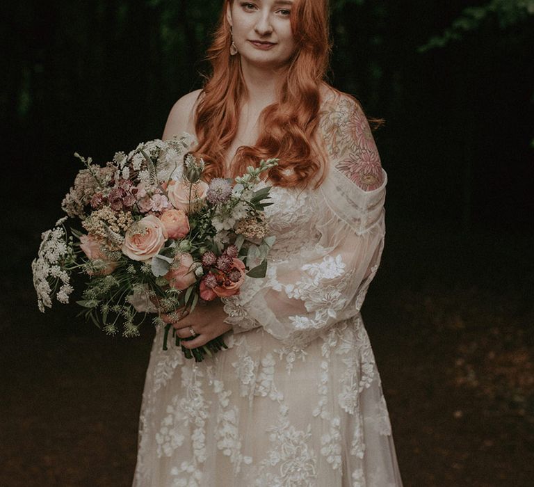 Bride in off the shoulder boho floral lace wedding dress holding pink flower bouquet 