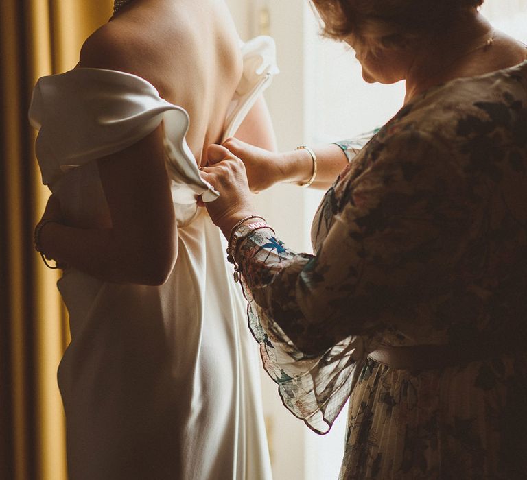 Mother of the bride helps the bride get ready for her wedding day by doing up the Vivienne Westwood wedding dress 