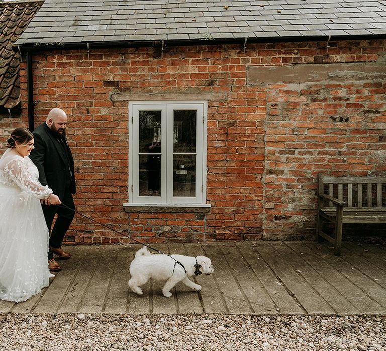 The bride and groom walk around the wedding venue with their pet dog 