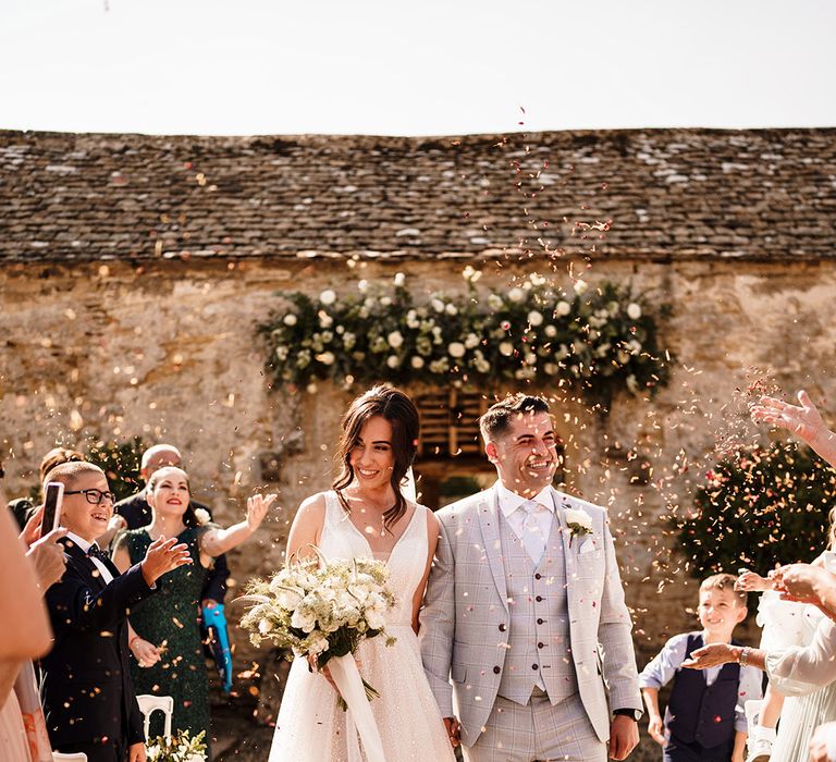 confetti moment at Caswell House outdoor wedding ceremony with bride in a sparkly princess wedding dress and groom in a light blue check wedding suit 