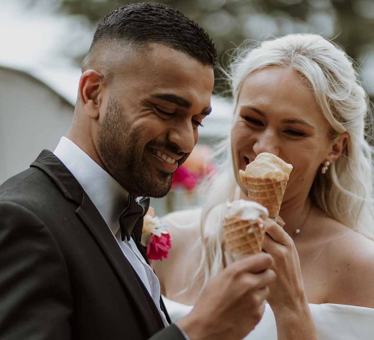 Groom in classic three piece grooms tuxedo with colourful spring boutonniere eating wedding ice cream with bride in off the shoulder lace wedding dress 