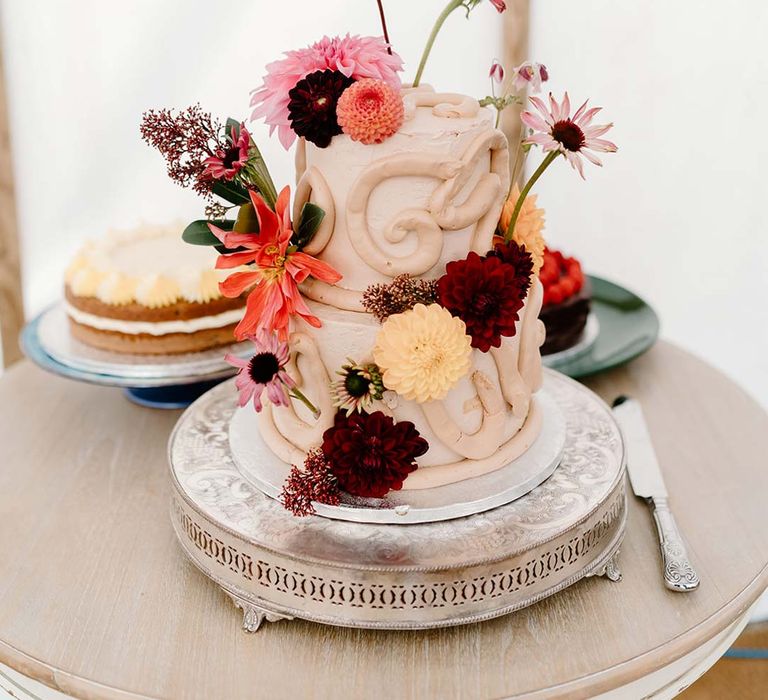 Small two tier off-white wedding cake with icing details and colourful edible flower decorations 