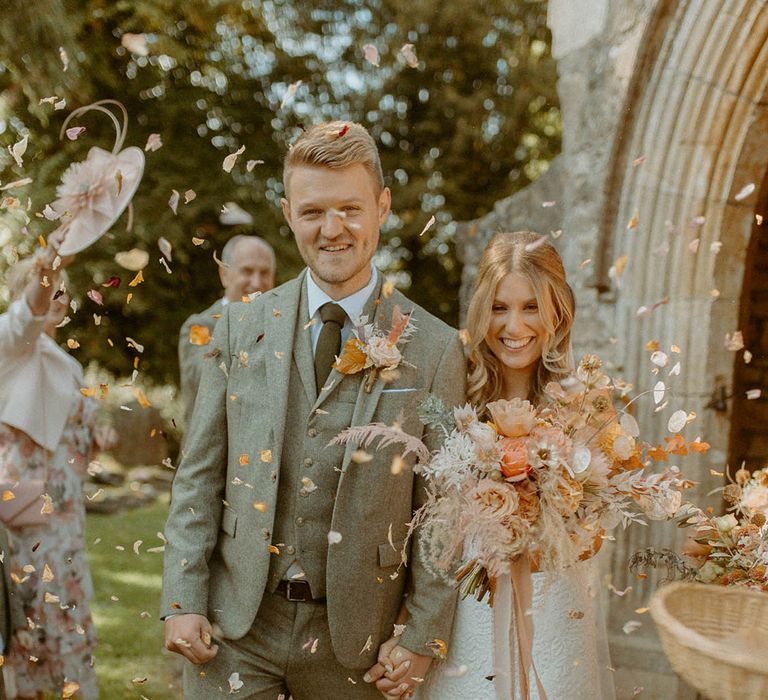 The bride and groom exit from their church ceremony with orange petal confetti 