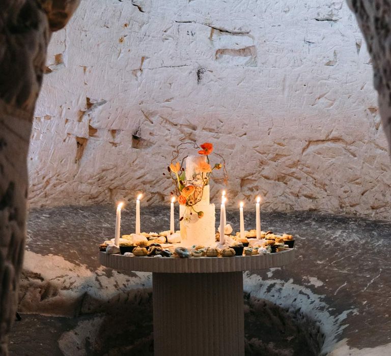 Three tiered iced wedding cake on wedding grazing table surrounded by tapered candles in Margate Caves