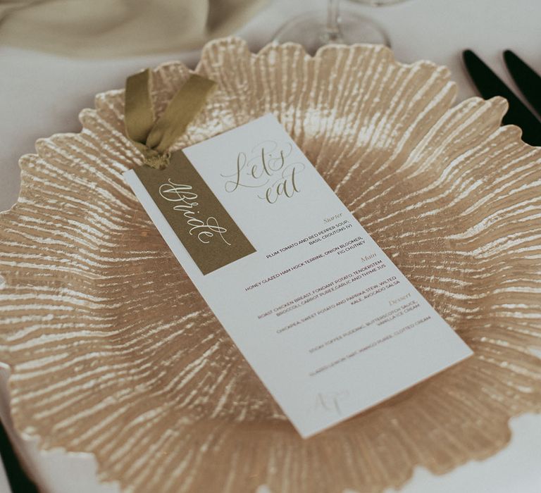 Gold and white wedding menu sign on sparkly gold charger plate 