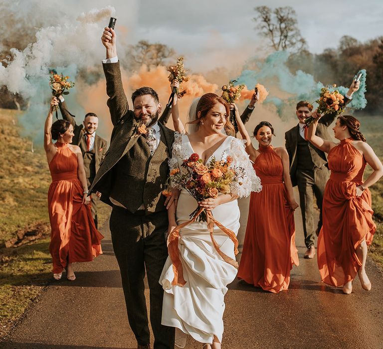 The bride and groom walk with their wedding party out to colourful smoke bombs exploding 