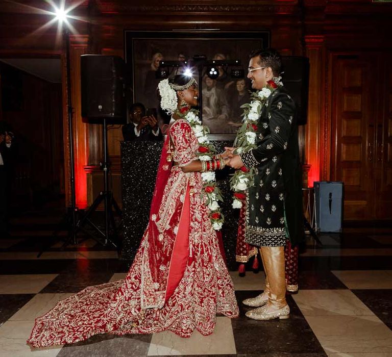 Groom in deep blue sherwani at Inner Temple Hall and garland standing with bride in red and gold bridal lehenga and garland following Inner Temple Hall vow renewal 