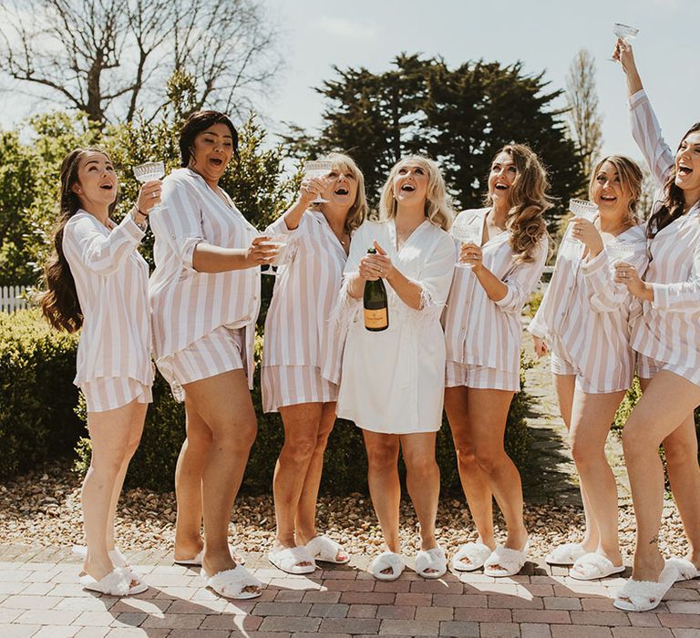 Bridal party in striped wedding pyjamas posing with the bride as they pop champagne 