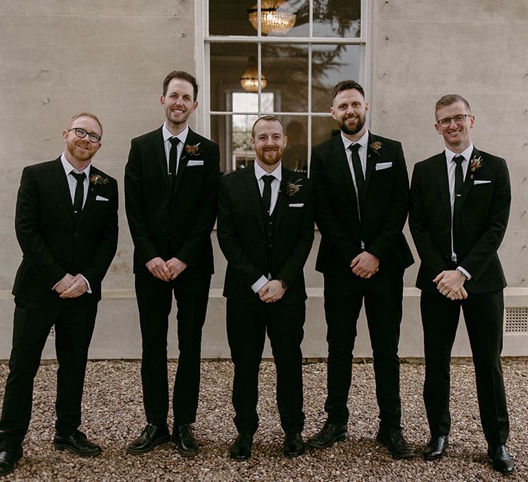 Groom and groomsmen wedding party photo with traditional black and white wedding suits with floral buttonholes 