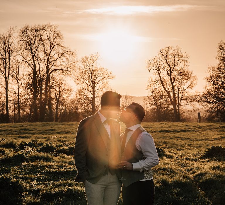 Stunning golden hour wedding photo at sunset with the two grooms gazing at each other 