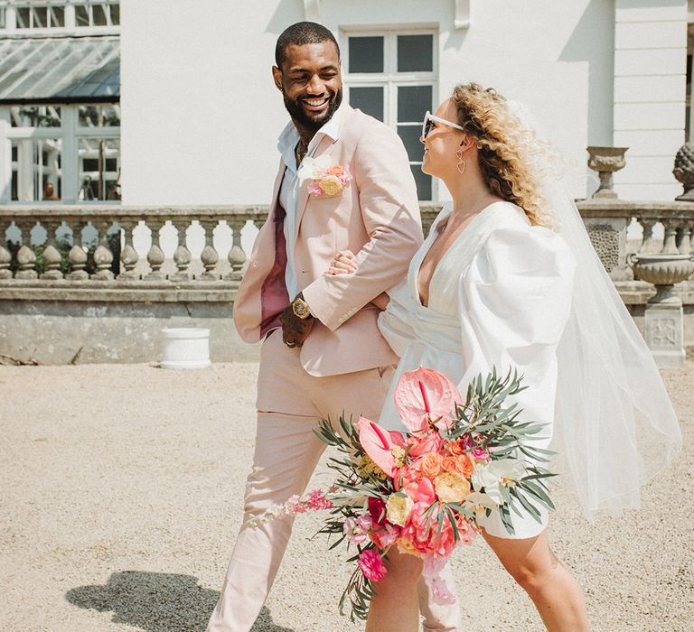 Bride in hot pink platform block heels for the wedding in a short wedding dress and groom in baby pink suit 