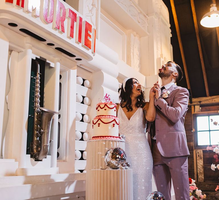 Bride and groom cutting their retros style wedding cake with pink and red icing decorating the white base 