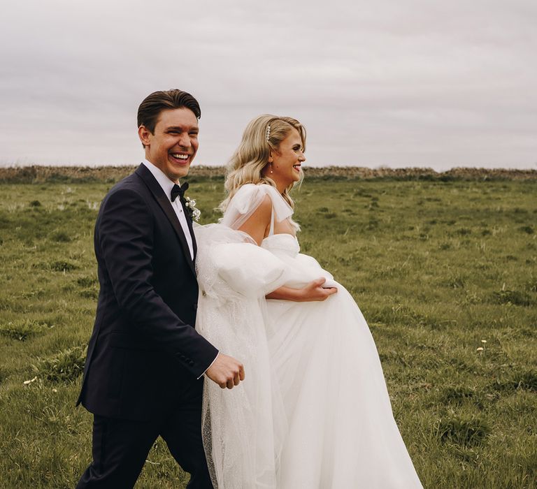 Groom in classic tuxedo walking hand in hand with the bride in a sparkly wedding dress with white trainers 