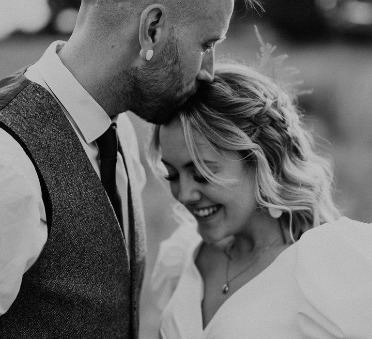 The groom kisses the bride on the head at their rustic festival wedding 