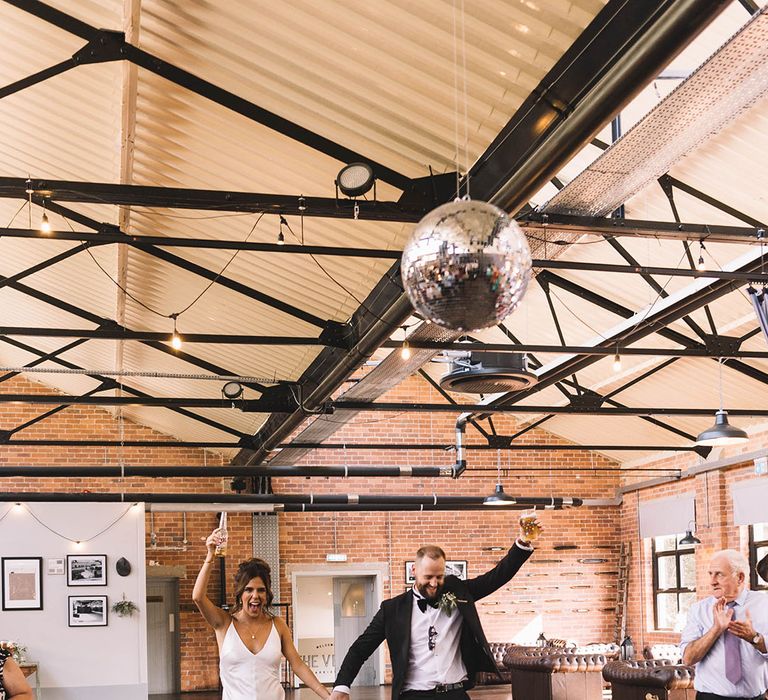 The bride and groom enter their wedding reception together with beer in hand 