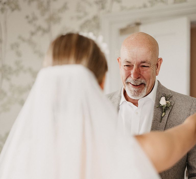 Father of the bride in beige stone coloured suit gets a first look at the bride during the morning of the wedding 