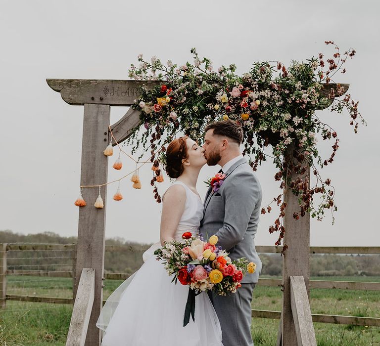 Hardwick Moat Weddings with wooden altar decoration with colourful flower decor as the bride and groom share a kiss 