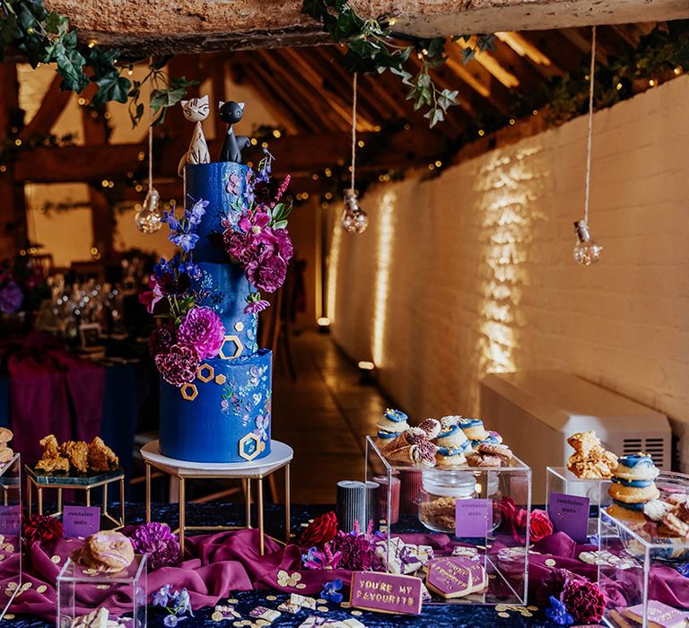 Bright and colourful three tier bright blue wedding cake decorated with pink and purple flowers and cat cake toppers 