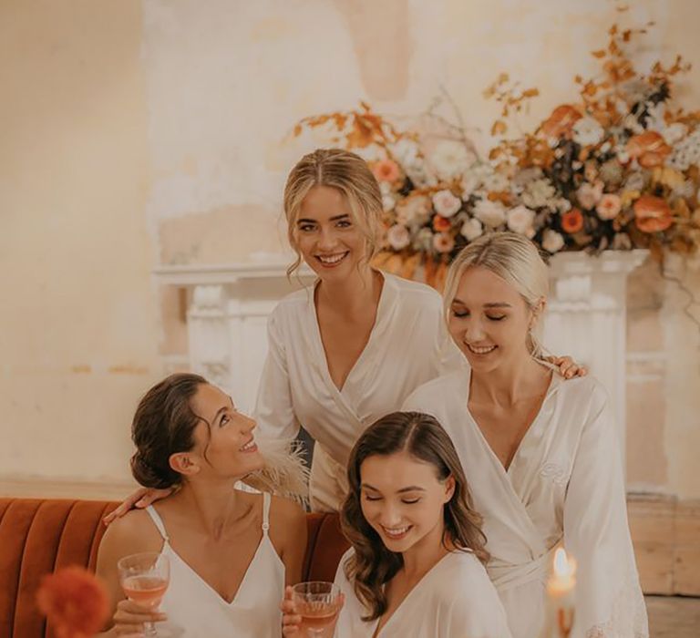 Four bridal party members wearing white satin pyjamas drinking bubbles by Pierra G Photography