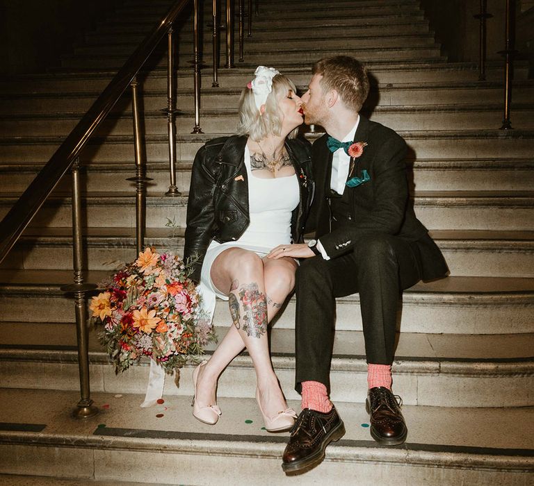 Bride wearing white headband and short wedding dress and black leather jacket with groom in black wedding suit 