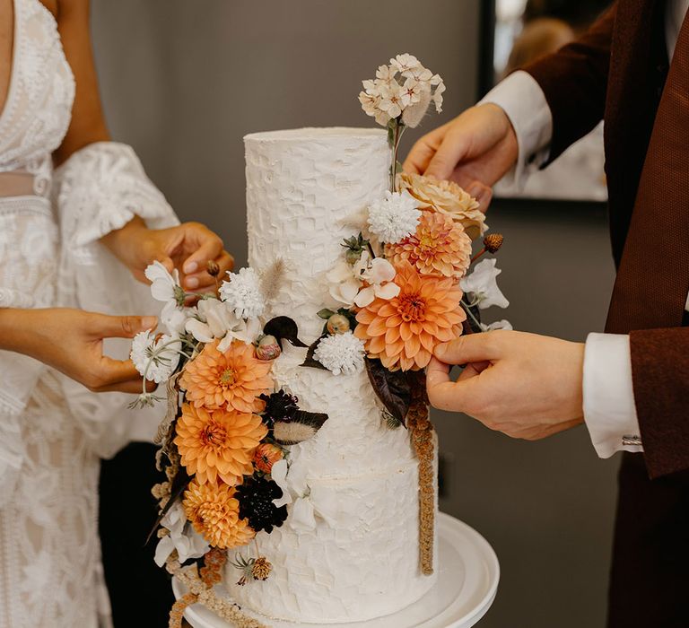 Three tier tall textured white iced wedding cake with orange and cream flower decorations 