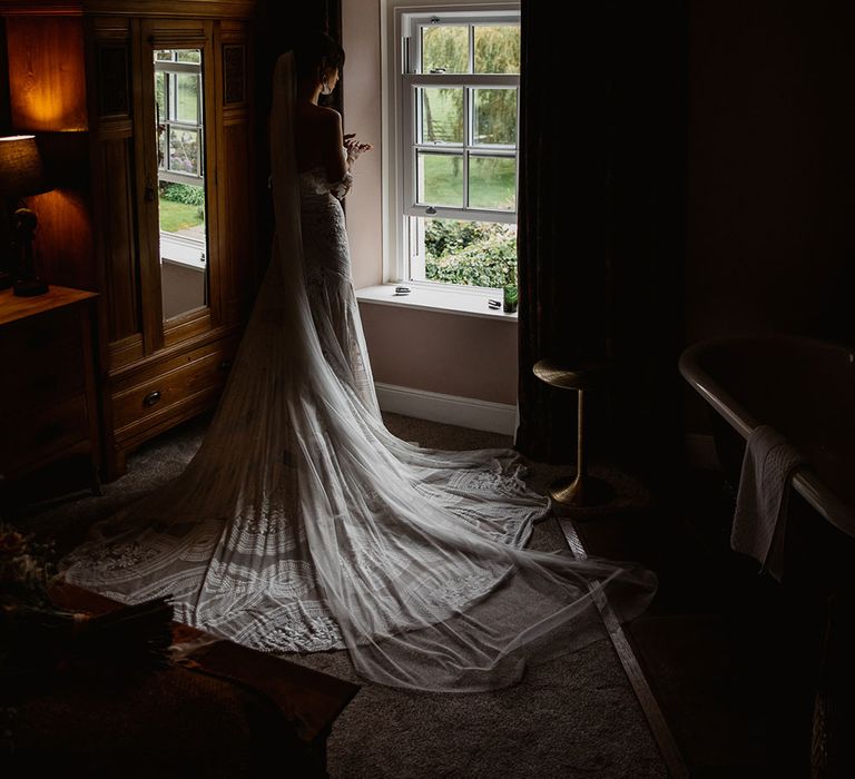 Bride in Rue de Seine wedding dress looks out the window