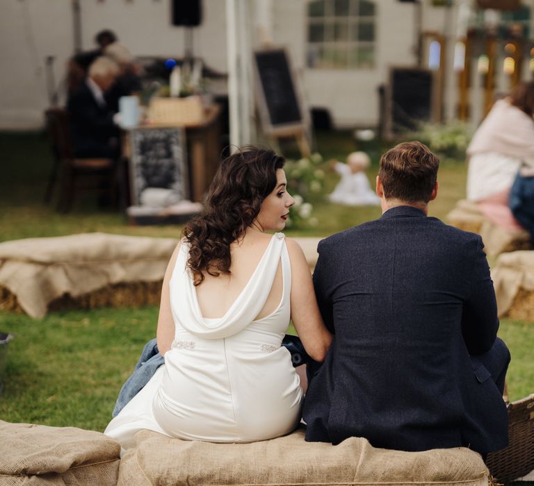 Bride & groom sit on hay bale at picnic 