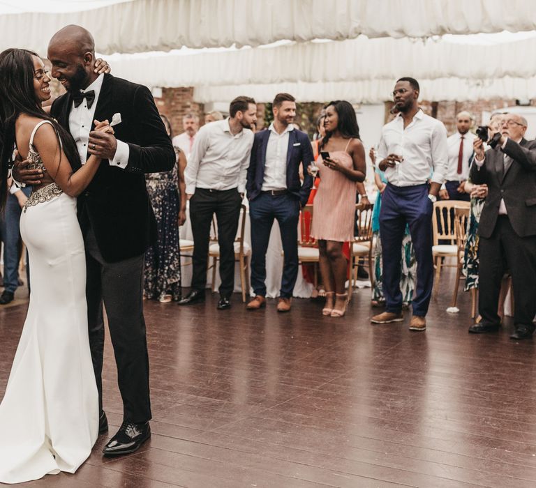 Wedding first dance with the Black groom in a velvet jacket leading his bride in a backless fitted wedding dress with low back detail 