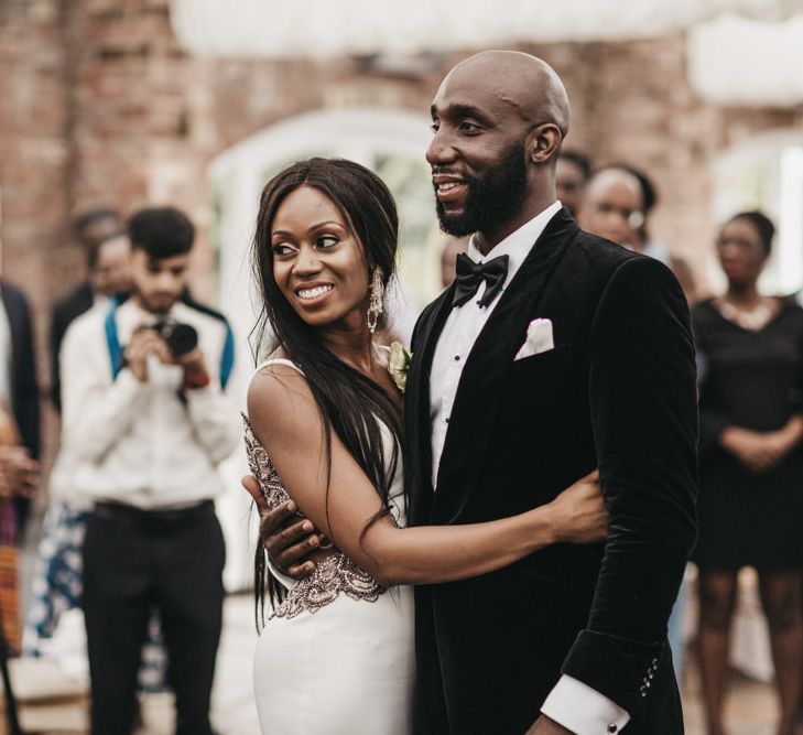 Black Bride with long hair embracing her husband in a velvet tuxedo jacket on the dance floor 