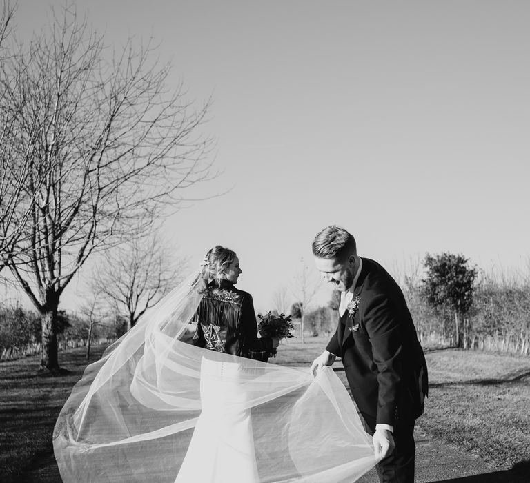 Black and white portrait of the groom adjusting his brides cathedral length wedding veil 