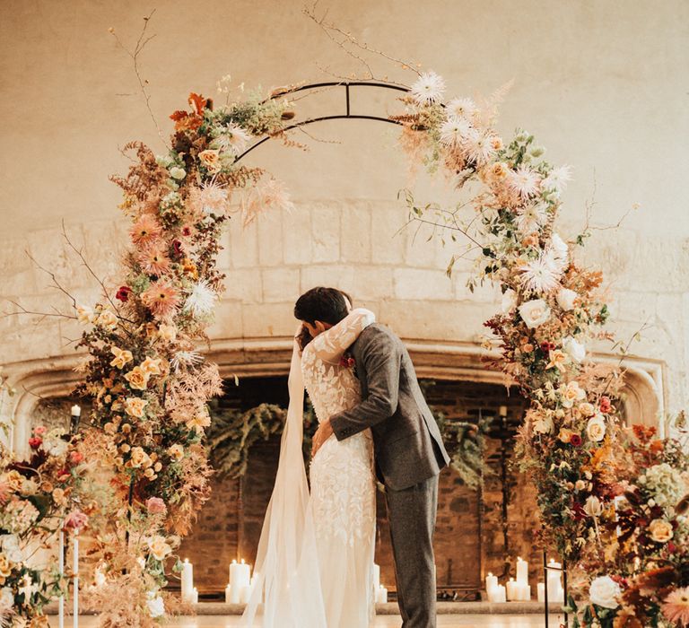 Bride in a lace Hermione De Paula wedding dress kissing the groom at the altar with orange and neutral wedding flowers 