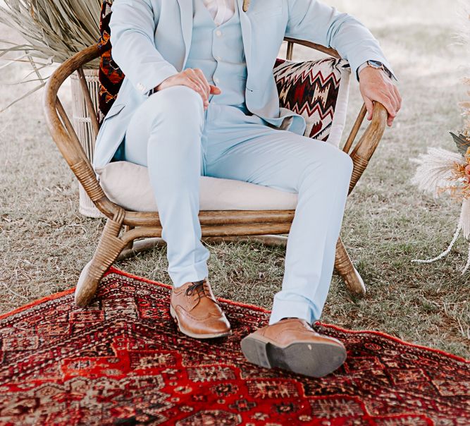 Groom sits back in wooden chair whilst wearing pastel blue suit