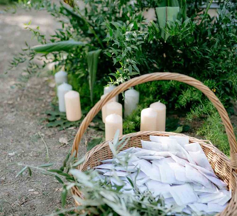 Candles and foliage surround a wicker basket with confetti pouches in 