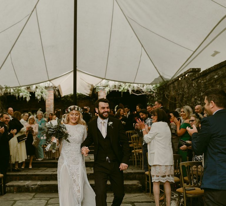 Bride in Grace Loves Lace wedding dress and single tier cathedral length veil walks down the aisle holding hands with groom in black Hugo Boss suit at Drenagh Estate Wedding