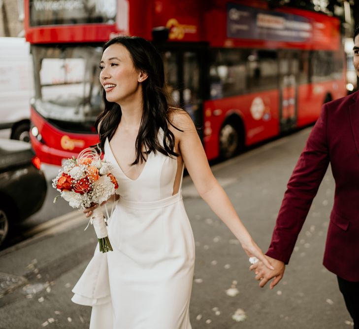 Bride and groom holding hands on the streets of London with a red double decker bus in the background 