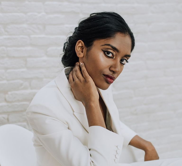 Bride wearing white bridal tailored suit with gold eyeshadow and bold eyeliner