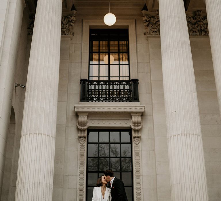 Bride & groom stand under pillars at the Old Marylebone Town Hall