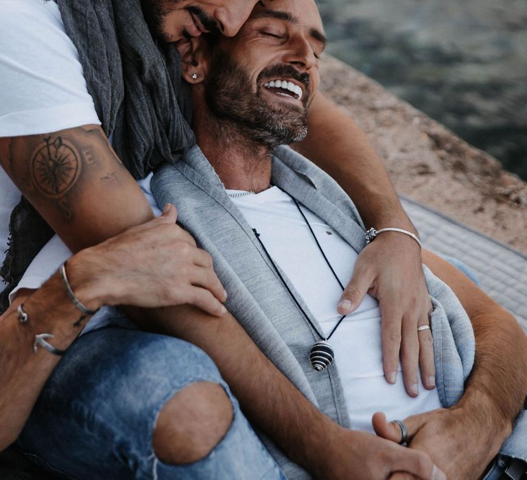 Groom leans back into boyfriend as they laugh together on the beach