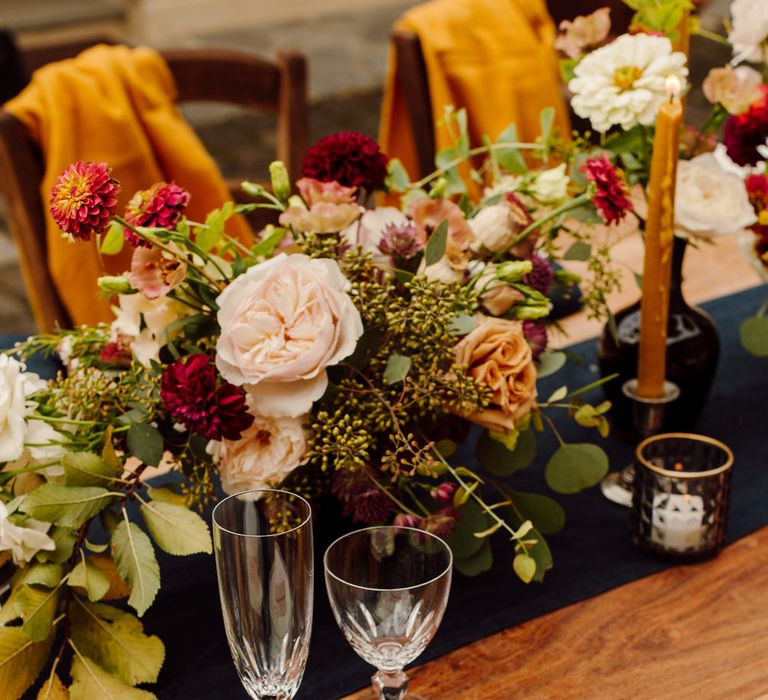 Wedding tablescape with centrepieces of roses, dahlias, eucalyptus leaves and wild grass. With blue linen napkins and simple name cards