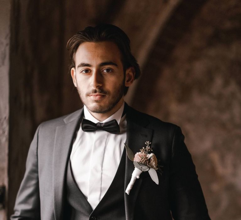 Groom wears black tie attire and stands with hands in pockets 