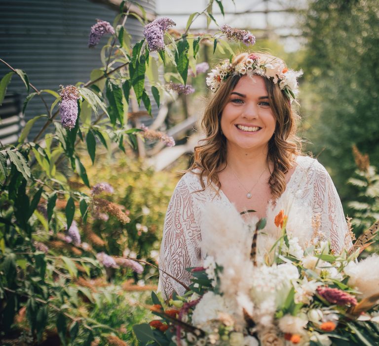 Bride smiles and wears flower crown surrounded by green foliage