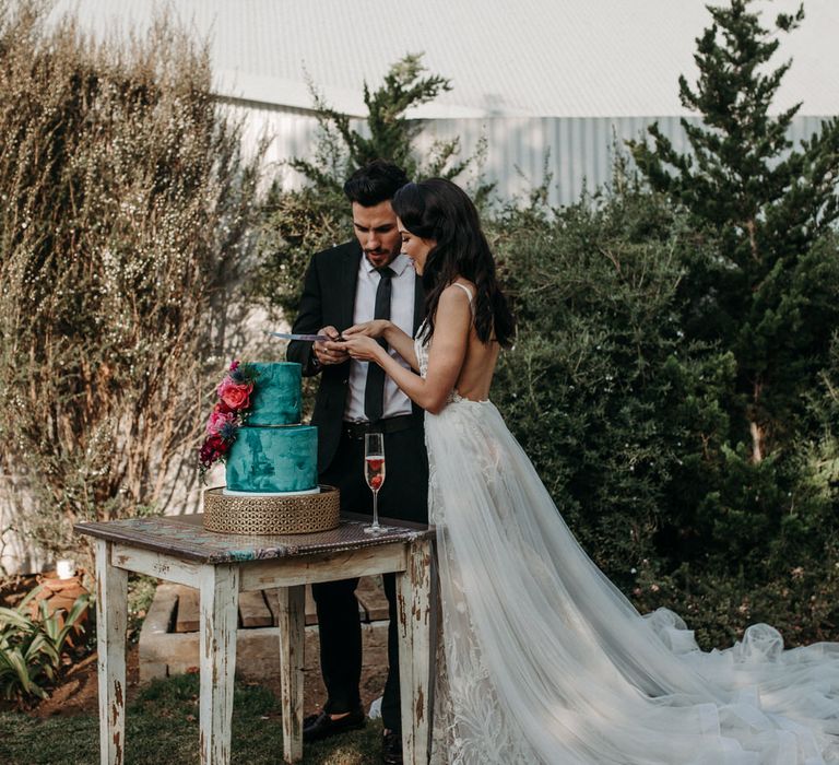 Bride and groom cutting their two tier turquoise wedding cake at outdoor rustic South African wedding