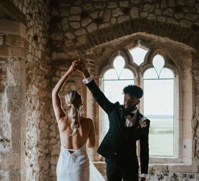 Groom in a black tuxedo twirling his bride in a low back Made With Love bridal gown 