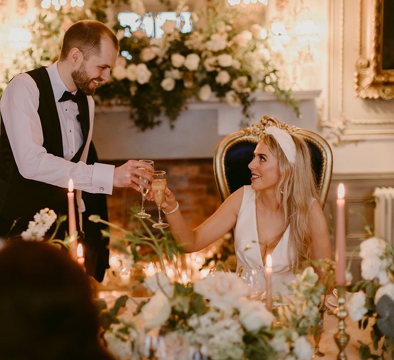 Bride & groom cheers with champagne during wedding reception surrounded by floral bouquets in classic styling