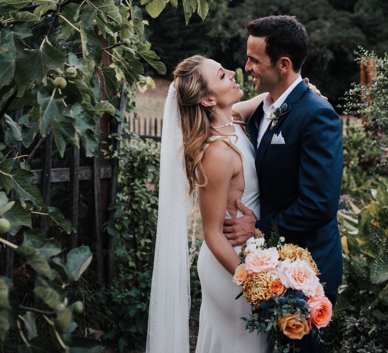 Bride & groom kiss outdoors against the green countryside